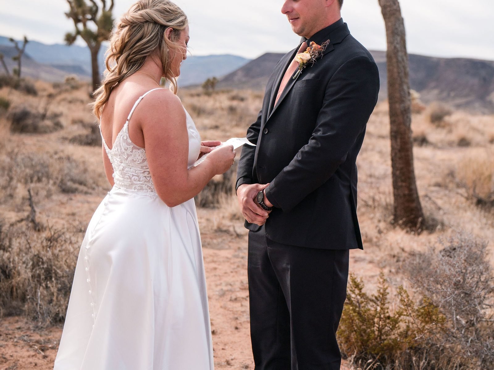 A bride reading to her groom from a card beside a Joshua tree