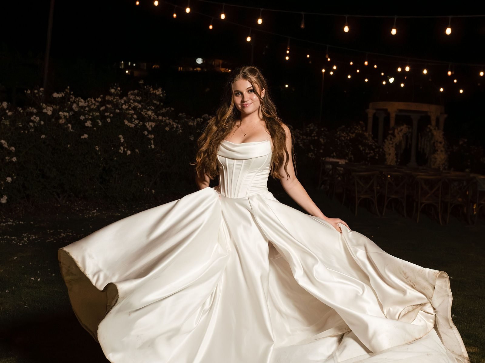 A bride spinning her gown on the lawn at night under string lights