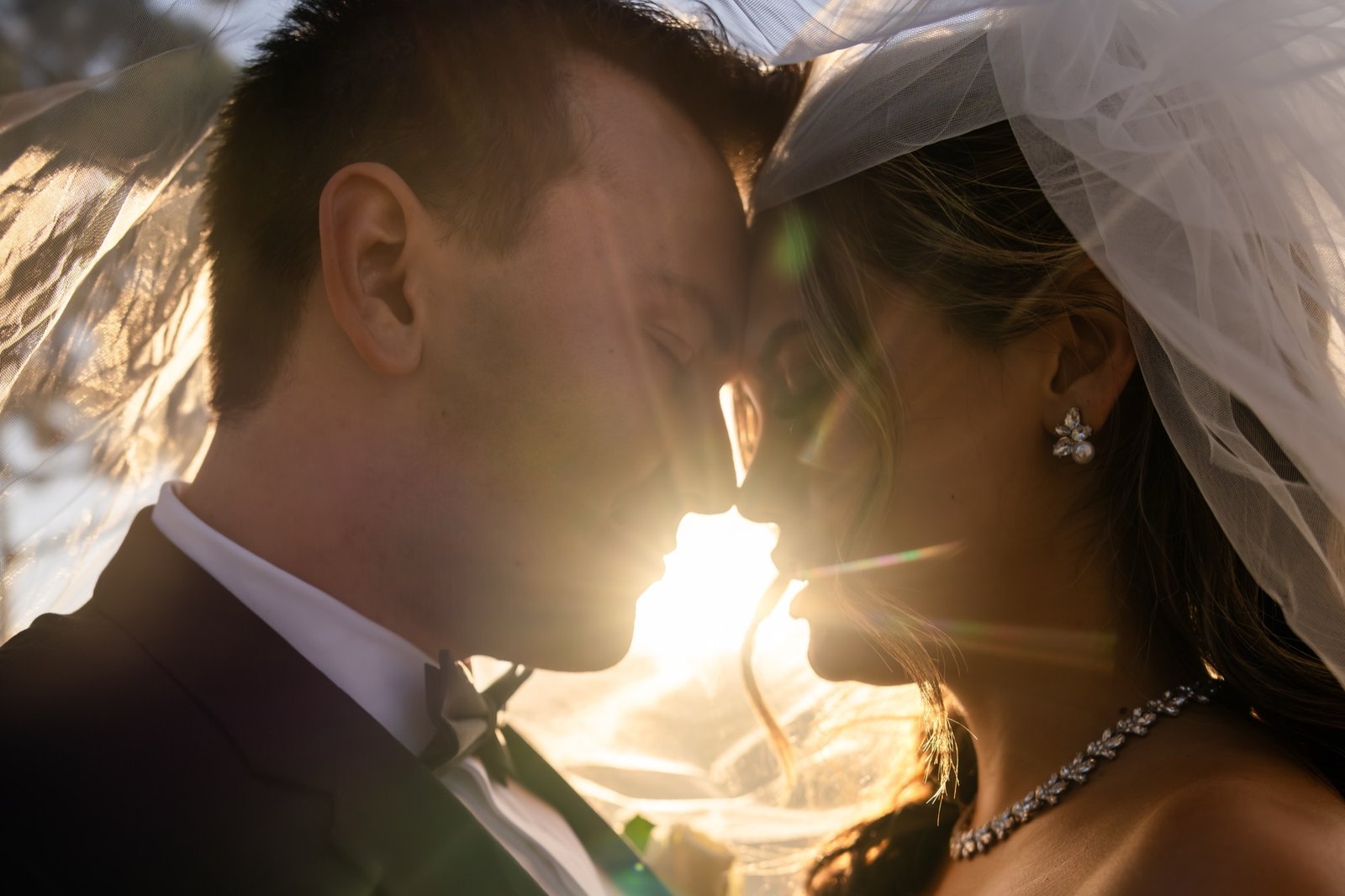 Leslie and Jonathan forehead to forehead under her veil with the sun behind them